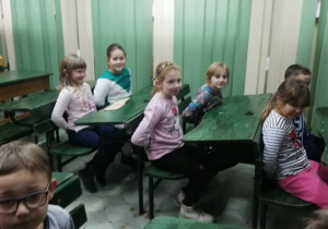 Dzieci w starych ławkach szkolnych.