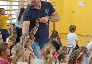 Prowadzący pokaz trzyma węża w ręku i daje go dotknąć uczniom.