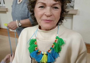 babcia przedstawiajaca swój naszyjnik zrobiony z włóczki w zielono niebieskiich koloroach